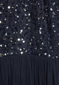 Tejido azul marino adornado con espirales de lentejuelas plateadas; texturado con una sección inferior de tul fruncido para mayor volumen y detalle.