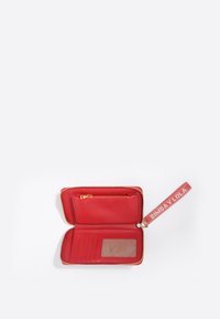 Cartera de cuero roja con cierre de cremallera, múltiples ranuras para tarjetas y una ventana transparente para identificación. Presenta una correa de marca para un fácil transporte.