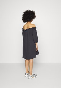 Vestido cinza escuro, à mostra dos ombros, com acabamento em babados e laços, apresentando mangas soltas e um comprimento de joelhos. Usado com ténis metálicos.