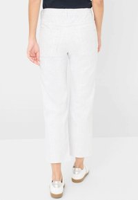 Pantaloni bianchi a coste a gamba larga con vita media e due tasche posteriori, abbinati a scarpe bianche con suola marrone.