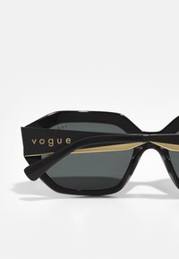 Mustad suurte mustade päikeseprillidega hallide objektiividega, kaheksanurkse kujuga, läikiva viimistluse ning kull värvi aktsenttriibuga, kus on "vogue" bränding käe peal.
