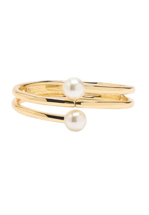 Złota bransoletka na podwójnym pasku z dwoma okrągłymi białymi perłami na otwartych końcach na białym tle.