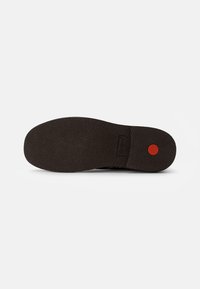 Sole in gomma nera con superficie testurizzata, accentuazione rossa rotonda e logo impresso. Forma piatta e arrotondata adatta per calzature casual.