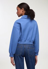 Felpa blu corta con colletto, orlo a coste e maniche a sbuffo, abbinata a jeans in denim scuro a vita alta. Texture liscia.
