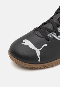 Zapatilla deportiva negra con un upper texturizado, cordones negros y el logo de Puma en blanco. Presenta una suela de goma marrón con un dibujo en relieve para mayor tracción.