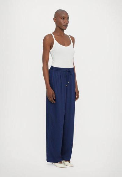 Navy wide-leg pants with an elastic waistband and drawstring, paired with a white fitted tank top. Smooth fabric with a relaxed fit.