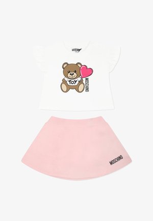 T-shirt bianco a maniche corte con maniche ruffle che presenta un orsetto cartoon e un cuore rosa. Gonna rosa con una cintura ampia e dettaglio con logo.