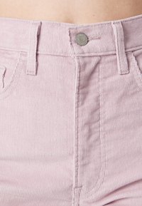Gros plan sur un pantalon en velours côtelé rose clair avec un bouton en métal et des passants de ceinture en haut de la taille.