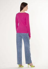 Maglietta rosa a maniche lunghe aderente con ampio scollo, abbinata a jeans blu in denim larghi e sandali verde con tacco. Tessuto morbido e design semplice.