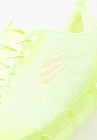 Světle zelená síťová sportovní obuv s lesklou průhlednou podešví, zdobená výrazným logem 'S' a texturovanými překryvy na svršku.