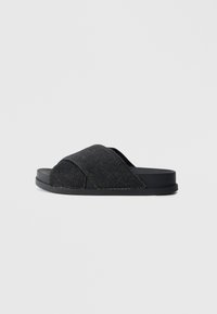 Sandale noire à glissière avec une tige en tissu denim, design à brides croisées, surface texturée et semelle noire plate et robuste.