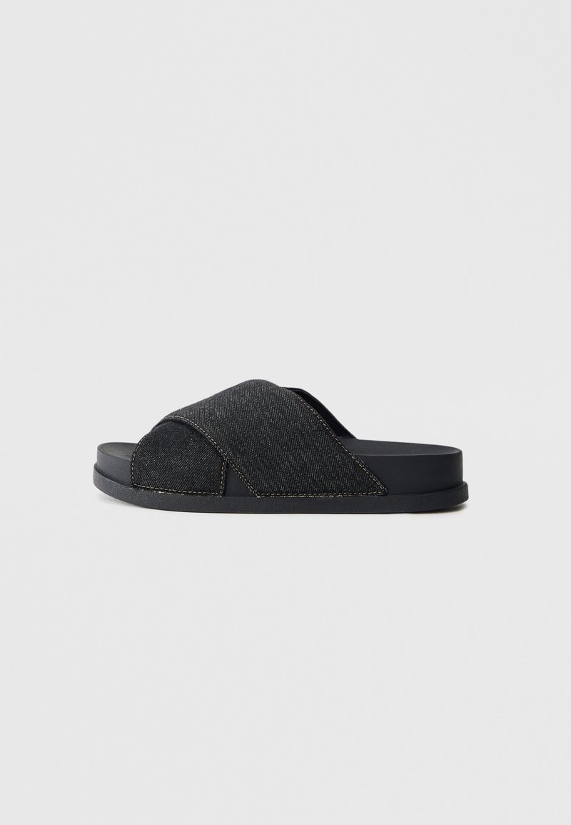 Sandale noire à glissière avec une tige en tissu denim, design à brides croisées, surface texturée et semelle noire plate et robuste.