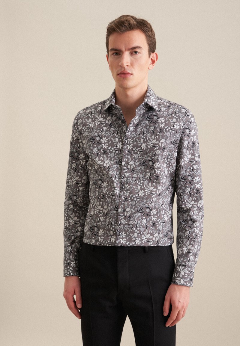 Koszula z długim rękawem w szarym materiale z kwiatowym wzorem w bieli i czerni. Posiada kołnierzyk w kształcie trójkąta oraz zapięcie na guziki z przodu.