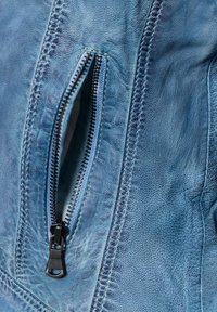 Helles blaues Ledergewebe im Close-up, das eine mit einem schwarzen Reißverschluss ausgestattete Tasche zeigt, mit Stichdetails entlang der Kanten.