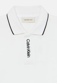 Fehér pamut póló gallérral, fekete színű gallérral és fekete hímzett "Calvin Klein" logóval. Címkék a gallér belső oldalán is találhatók.