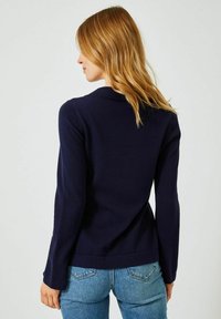 Marinblå långärmad tröja med en slät yta, krage och en kroppsnära passform, ihop med ljusblå tajta jeans.