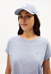 T-shirt di cotone lilla con maniche corte arrotolate, caratterizzata da un piccolo logo ricamato sul lato sinistro del petto. Cappello abbinato di colore lilla.