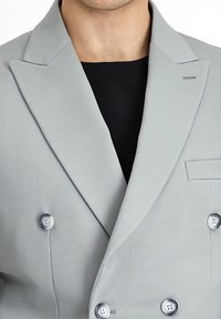 Jasnoszara, dwurzędowa marynarka o fakturowanej tkaninie, z klapami w kształcie szpica i srebrnymi guzikami. Posiada kieszeń na piersi i dwa przednie guziki.