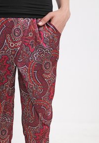 Röda och rosa paisleymönstrade byxor med en slät textur och sidofickor, med intrikata blommiga och cirkulära mönster på tyget.