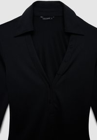 Chemise noire à boutons avec col en V, fabriquée dans un tissu lisse, comportant six boutons sur la patte de boutonnage et un design décontracté.