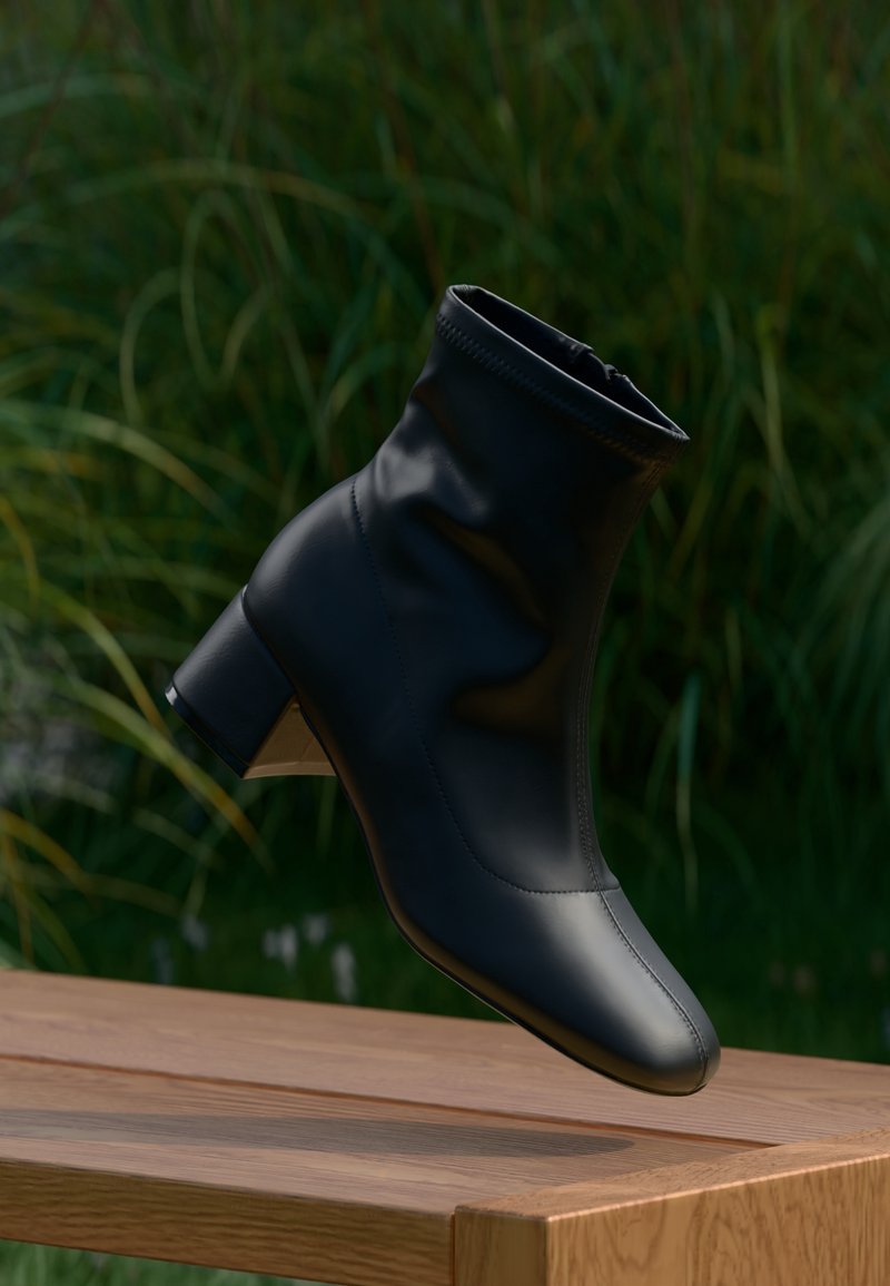 Bottine noire en cuir à talon bloc flottant au-dessus d'un banc en bois, avec un feuillage vert en arrière-plan.
