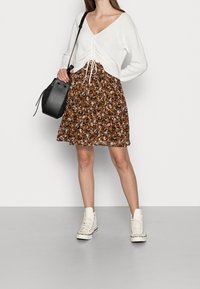 Valkoinen pitkähiha-toppu, jossa on kiristettävä vyötärö, yhdistettynä ruskeaan leopardikuvioiseen hameeseen ja valkoisiin korkeisiin tennareihin. Musta käsilaukku täydentää asun.