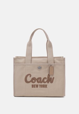 Beżowa torba typu tote z płótna z podwójnymi uchwytami, przednią kieszenią, zamknięciem na obrotowy zamek oraz logo "Coach New York" w brązowych literach.
