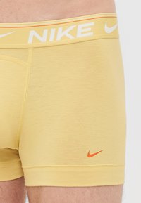 Gele boxershorts gemaakt van zachte stof. Witte elastische tailleband met oranje accenten en het "Nike" logo. Korte beenlengte.