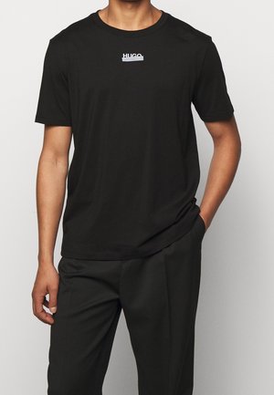T-shirt in cotone nero con maniche corte, caratterizzato da un logo bianco con la scritta "HUGO" sul petto. Tessuto morbido, vestibilità classica.