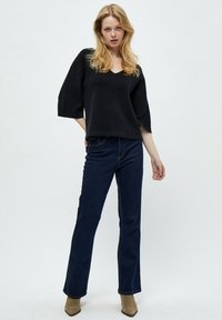 Maglione nero, in forma ampia, con scollatura a V e maniche larghe, abbinato a jeans svasati blu scuro e stivali alla caviglia marrone chiaro.