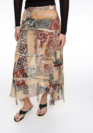 Mujer con falda midi de varias capas y múltiples estampados, con diseños florales y abstractos, combinada con una blusa de manga larga negra y sandalias negras de tacón con punta abierta.