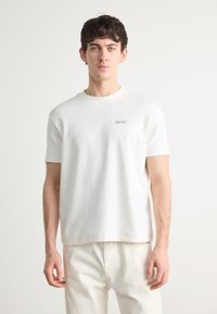 Baltas apvalios iškirpės marškinėliai, pagaminti iš minkštos medvilnės. Turi trumpas rankoves ir mažą raudoną Calvin Klein logotipą ant krūtinės. Paprastas dizainas.
