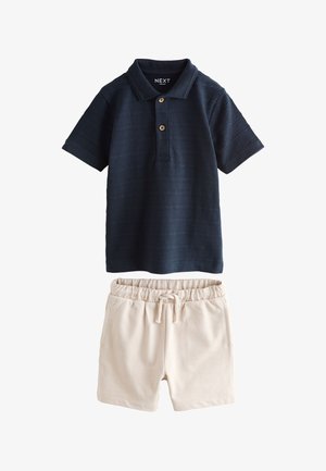 Tengerészkék rövid ujjú galléros póló, két gombbal, bézs elasztikus derékpántos rövidnadrággal, húzózsinórral és oldalzsebekkel párosítva.