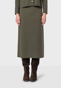 Gonna a maglia verde oliva, lunga fino al ginocchio, abbinata a stivali alti in suede marrone. La gonna presenta una finitura liscia e strutturata.