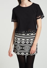 Top nero a maniche corte con bordo trasparente abbinato a una gonna mini a righe nera e bianca, aderente, caratterizzata da design geometrici e strisce orizzontali.