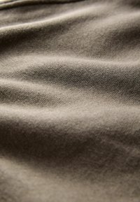 Dettaglio ravvicinato della trama di un tessuto beige che mostra un fine intreccio e morbide pieghe che creano ombre leggere.