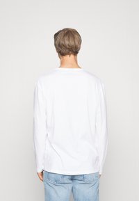 Weißes Langarm-T-Shirt mit Rundhalsausschnitt, aus Baumwolle, mit geradem Schnitt und minimalen Nähten, kombiniert mit hellblauen Jeans.