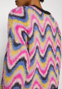 Maglione soffice con un motivo a zigzag in rosa, blu, giallo e nero; il tessuto testurizzato aggiunge profondità e interesse visivo.