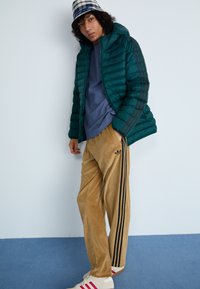 Casaco acolchoado em teal com capuz, t-shirt azul, calças de corduroy em tom areia com riscas pretas e ténis brancos com detalhes em vermelho.