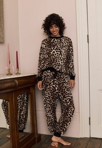 Súprava loungewear s leopardím vzorom vyrobená z mäkkého materiálu, obsahujúca voľný vrch a zúžené nohavice s čiernymi akcentmi a elastickými manžetami.