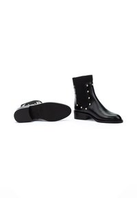 Botas de tobillo de cuero negro con parte superior de tela acanalada, tachuelas de metal en los lados, suela de cuero plana y tacón bloque estrecho.