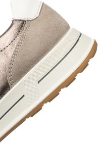 Close-up of a sneaker heel with beige suede, metallic bronze accents, white midsole, and gum rubber outsole.