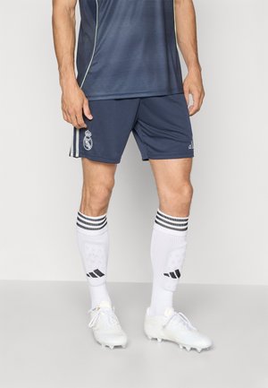 „Adidas Real Madrid“ vyriški futbolo marškiniai, turintys laivyno mėlynumo trumpas rankoves, derančius šortus, baltas kelių kojines su juodais dryžiais ir baltus sportbačius.
