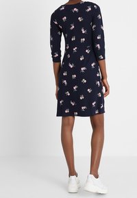 Mörkblå klänning med 3/4-ärmar, med ett blommönster i rosa och grönt. Knä-lång design med avslappnad passform, kombinerad med vita sneakers.