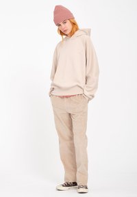 Beige hoodie met ribbeltrimming, gecombineerd met lichtbeige corduroy broek en bruine sneakers. Model draagt een lichtroze gebreide beanie.