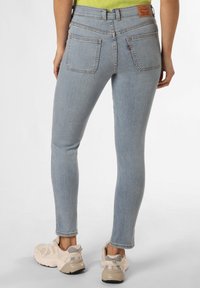 Vaqueros skinny de color azul claro con cintura alta, costuras delineadas y dos bolsillos traseros; combinados con zapatillas deportivas beige.