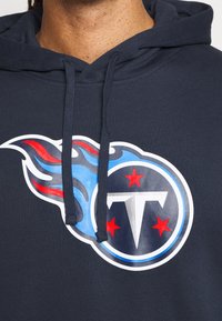 Felpa con cappuccio blu navy caratterizzata da una grande grafica del logo di una squadra sportiva, con stelle rosse e fiamme blu, realizzata in un tessuto morbido con una superficie liscia.