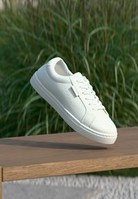 Weiße Sneakers aus glattem, synthetischem Material, mit Schnürverschluss, runder Zehenpartie, subtilen Perforationen und einer strukturierten Gummisohle.