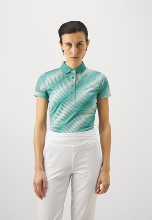 Türemansche Polohemd in Blaugrün mit Kragen, das diagonale weiße Streifen aufweist; kombiniert mit weißen hoch taillierten Hosen. Glattes, leichtes Material.