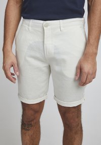 Pantalones cortos de color beige claro, confeccionados en una mezcla de lino, con dobladillo enrollado, cierre de botón y dos bolsillos laterales con una superficie texturizada.